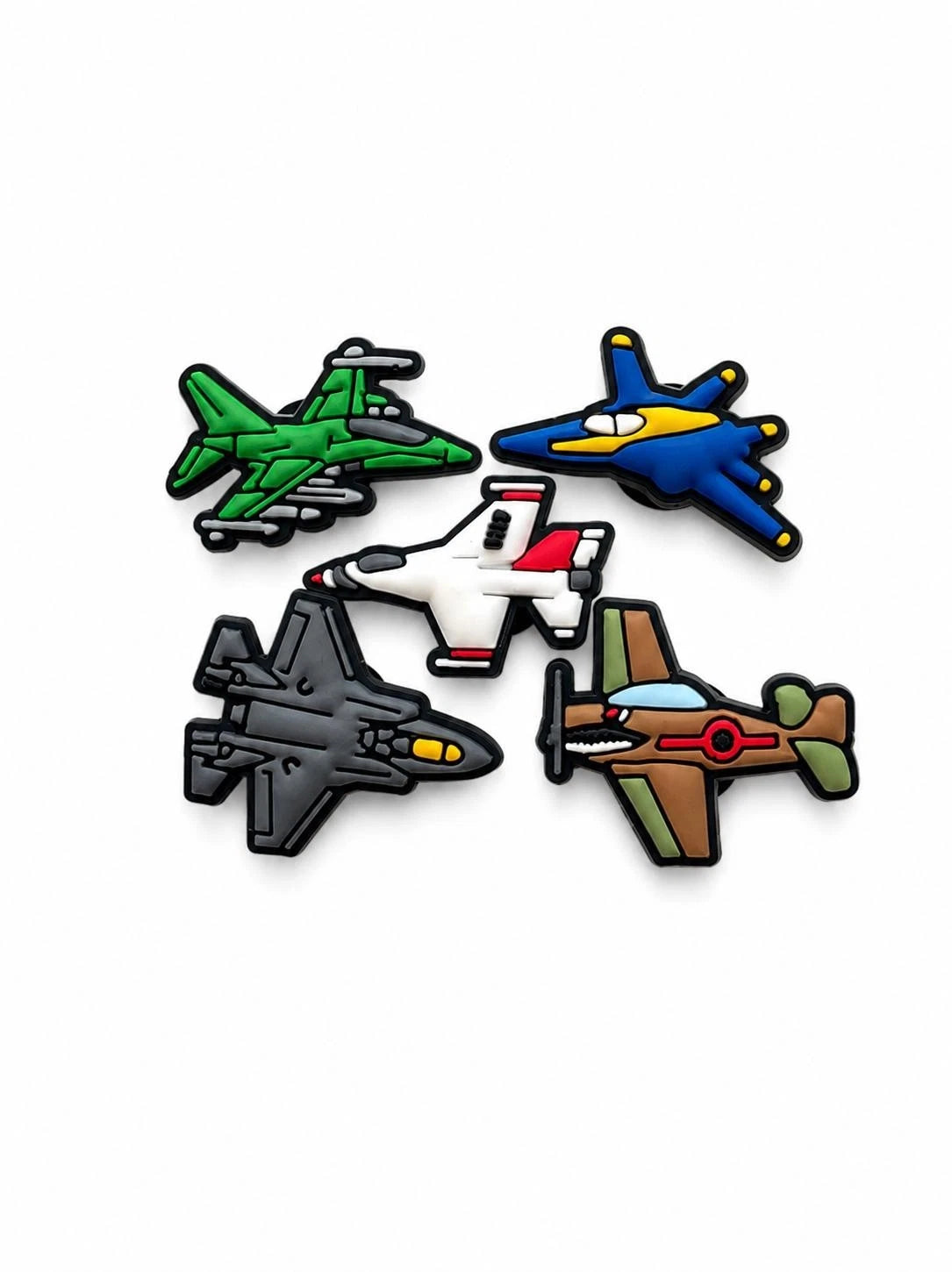 Five cartoon-style airplane charms or patches arranged on a plain white background. The designs include a green jet, a blue fighter plane, a white and red jet, and a brown military-style plane with olive green wings.